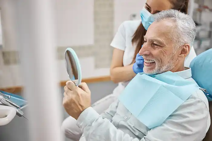 A smiling dental patient with a mirror observing their teeth at Rocket City Prosthodontics 